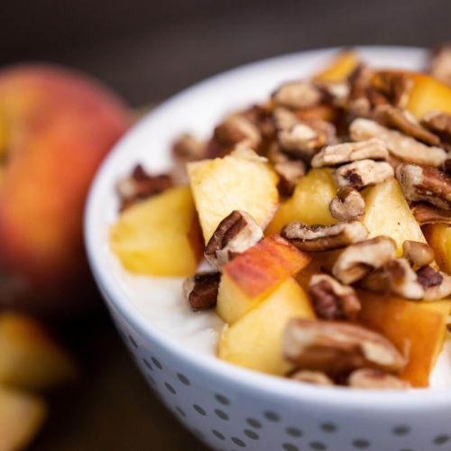 Bowl of yogurt topped with chopped peaches and pecans.