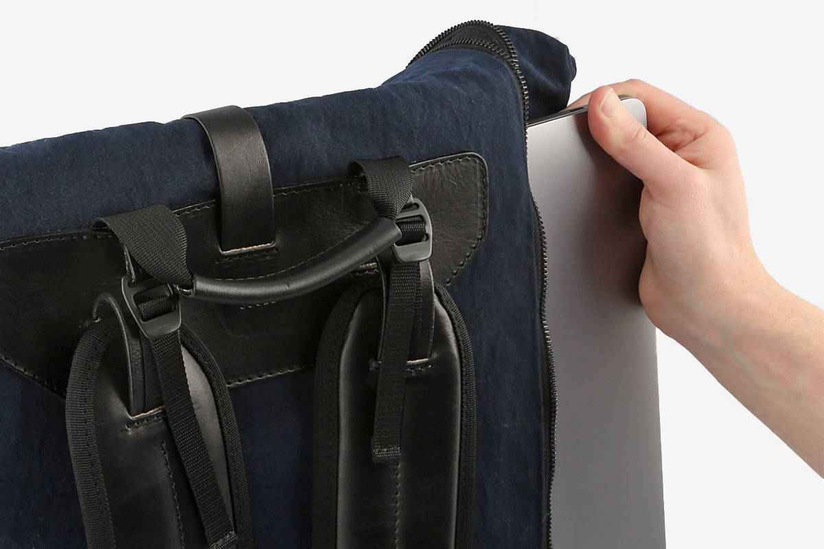 Pulling a Macbook out of the side of a navy blue backpack.