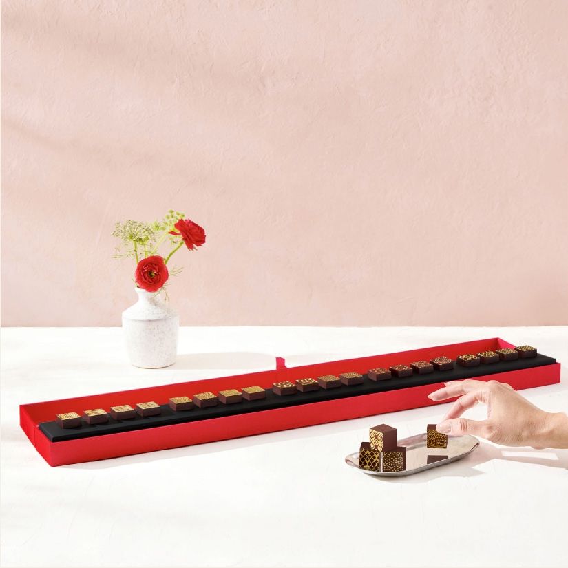A hand reaching for chocolates on a red tray with flowers in the background.