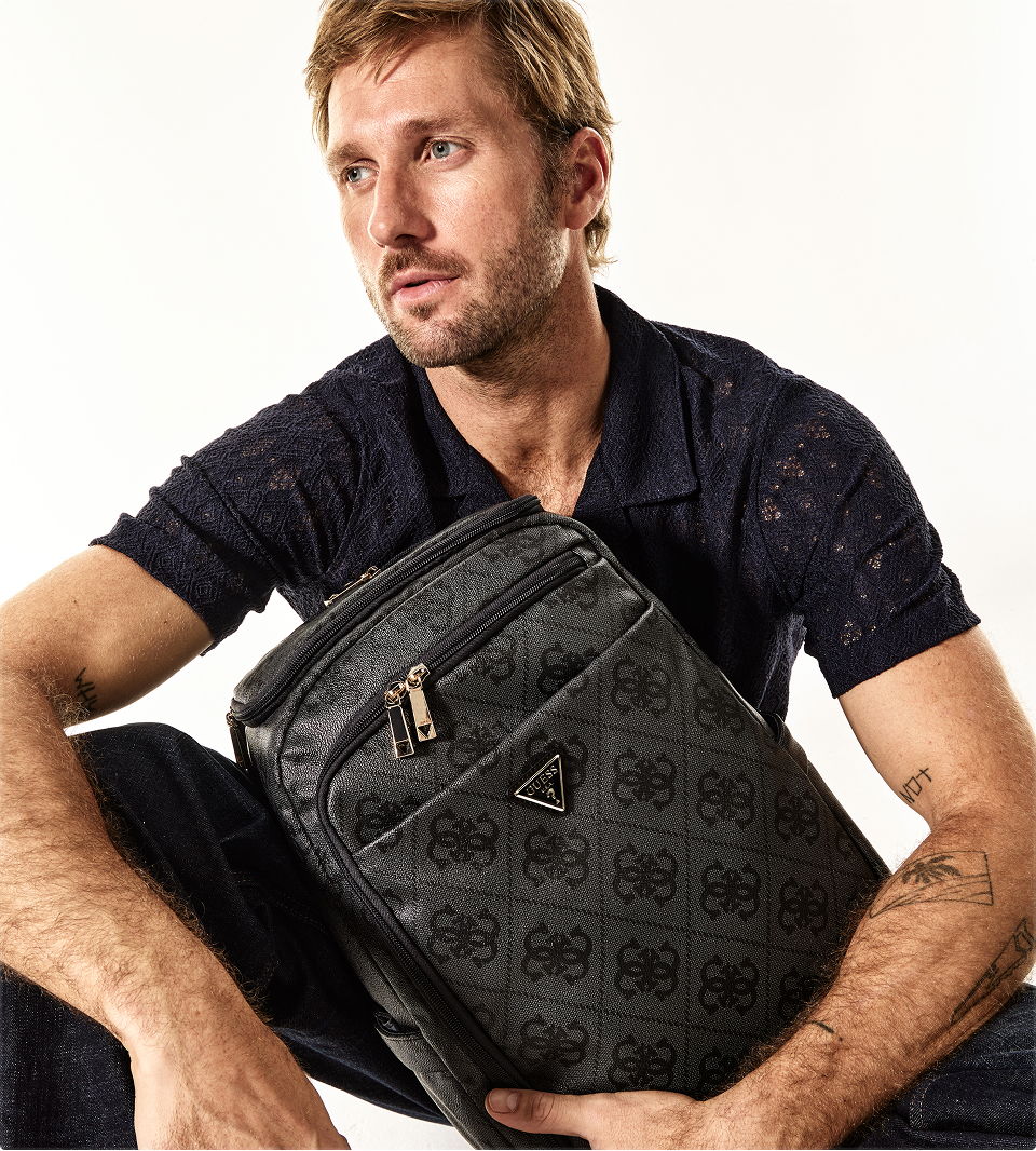 Man sitting with a GUESS backpack, wearing a dark polo shirt.