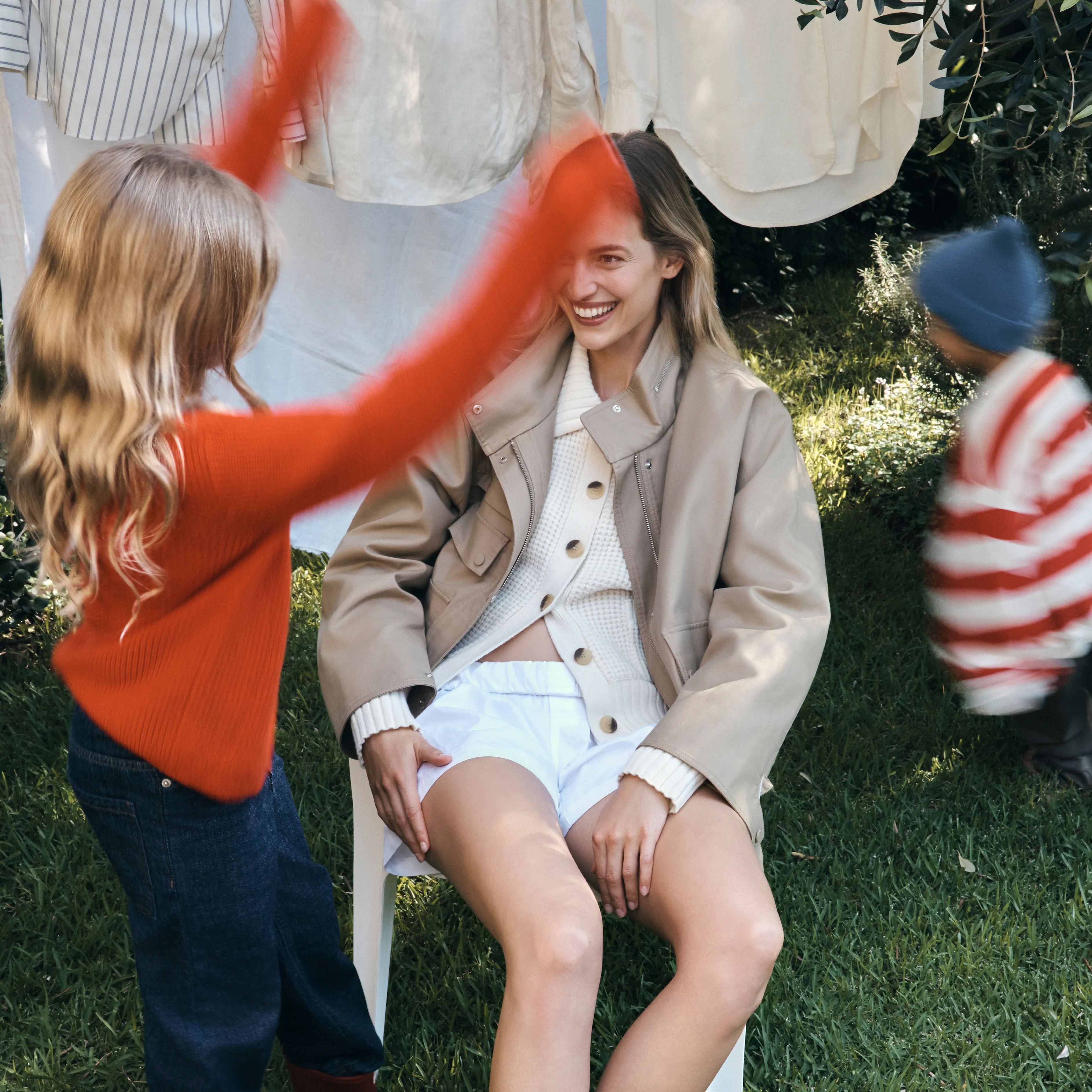 A girl plays joyfully near a seated woman outdoors.