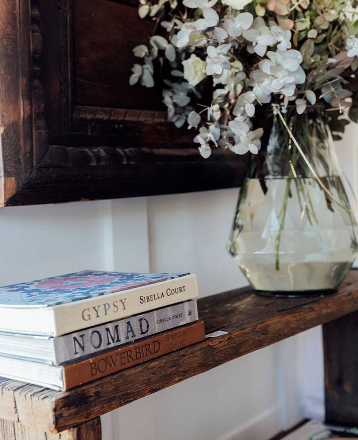 Three books on a wooden entryway table with glass vase 