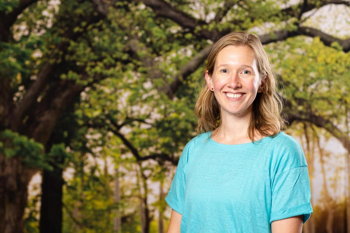 Smiling woman in a blue shirt standing in front of trees.