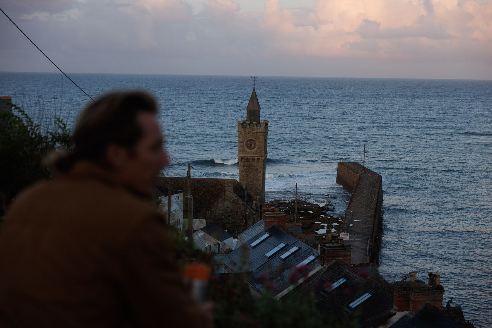 Person overlooking a coastal town with a clock tower and ocean in the background.