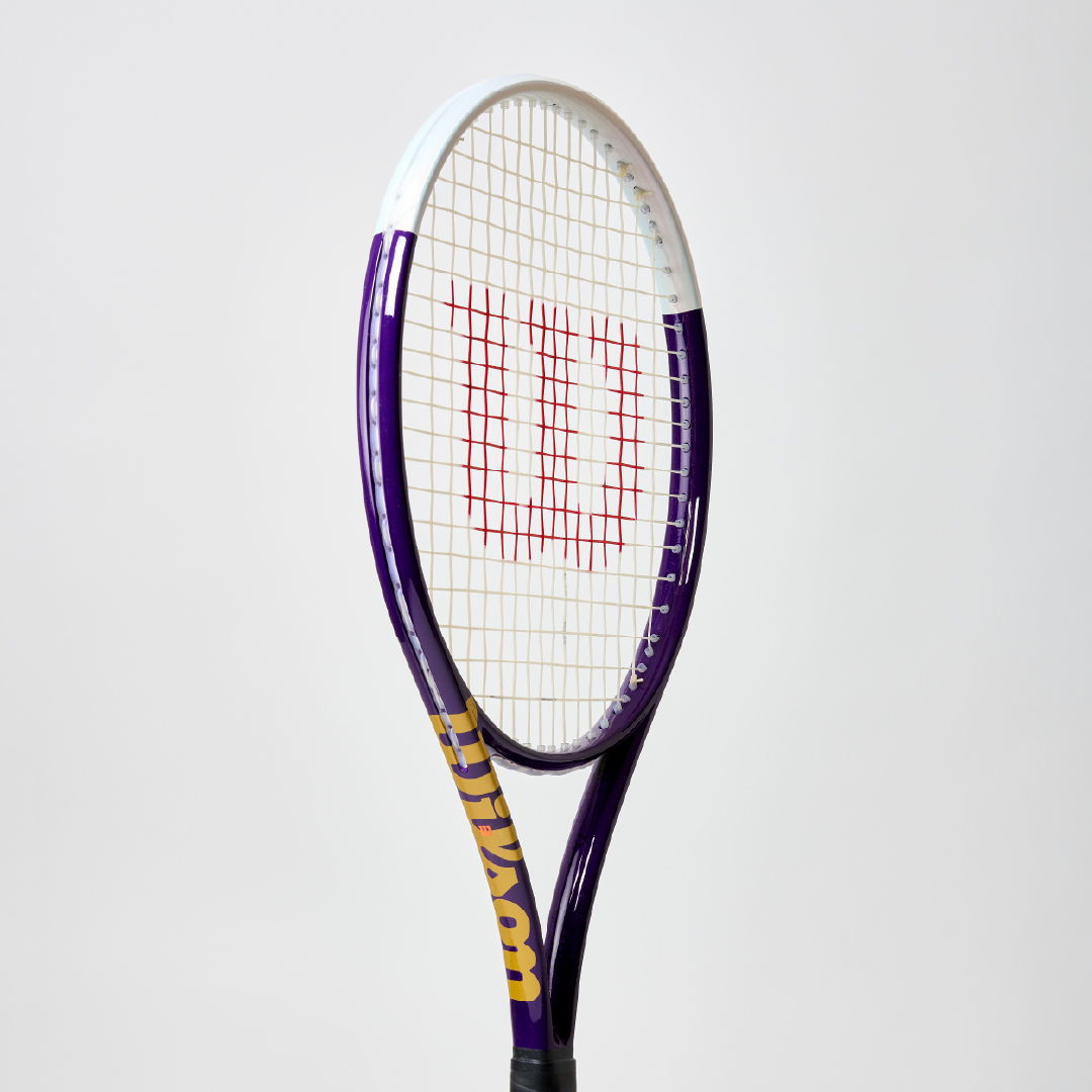 Tennis racket with a purple frame and red strings against a white background.