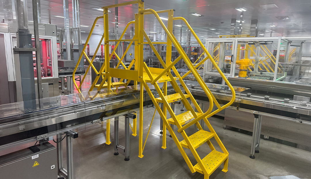 Custom conveyor crossover platform with two entry and exit points providing elevated passage over production conveyors in a manufacturing facility