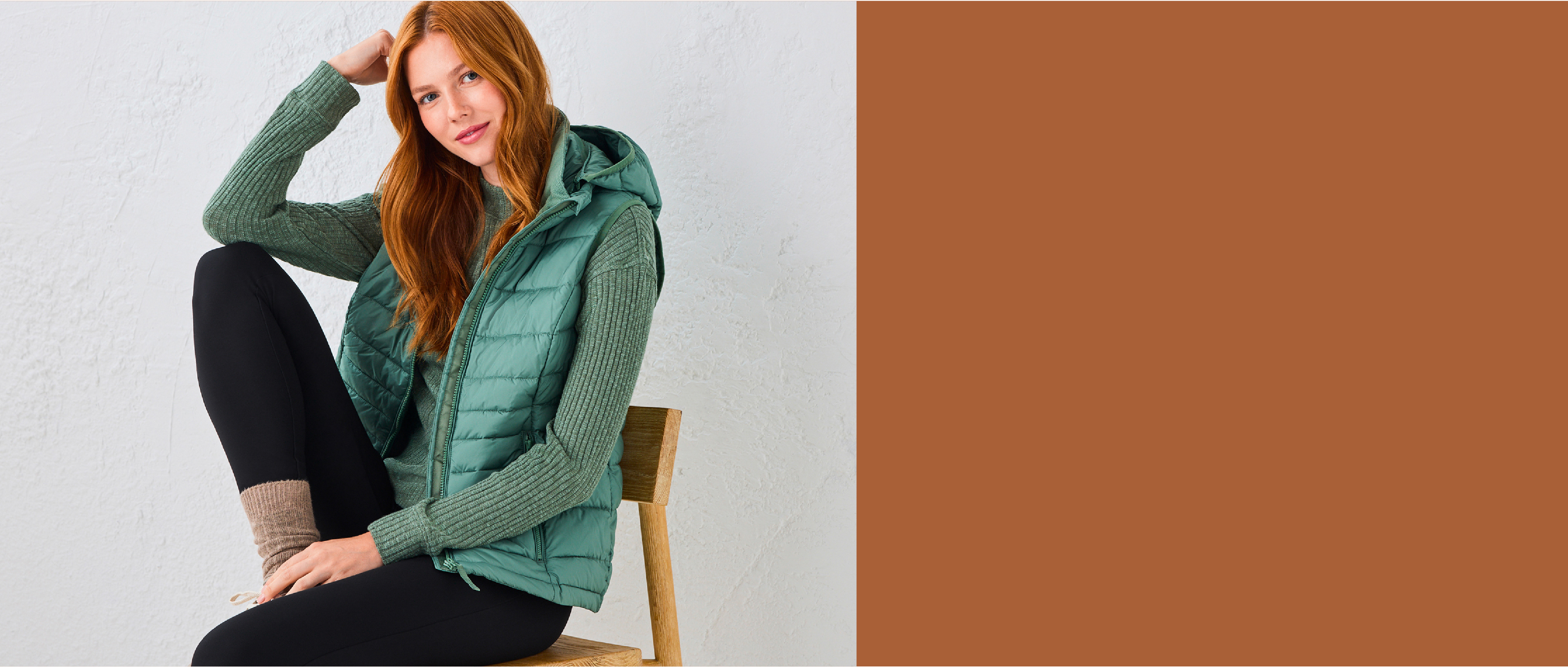 Woman wearing a green vest sitting on a chair against a plain background.