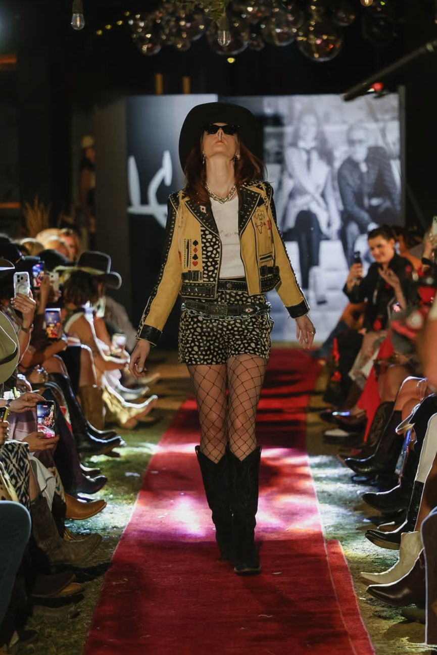 Model Clarissa Jane wearing the Cowboy Graffiti Jacket and Howdy Dotty shorts as she walks down the runway smoking a cigarette.