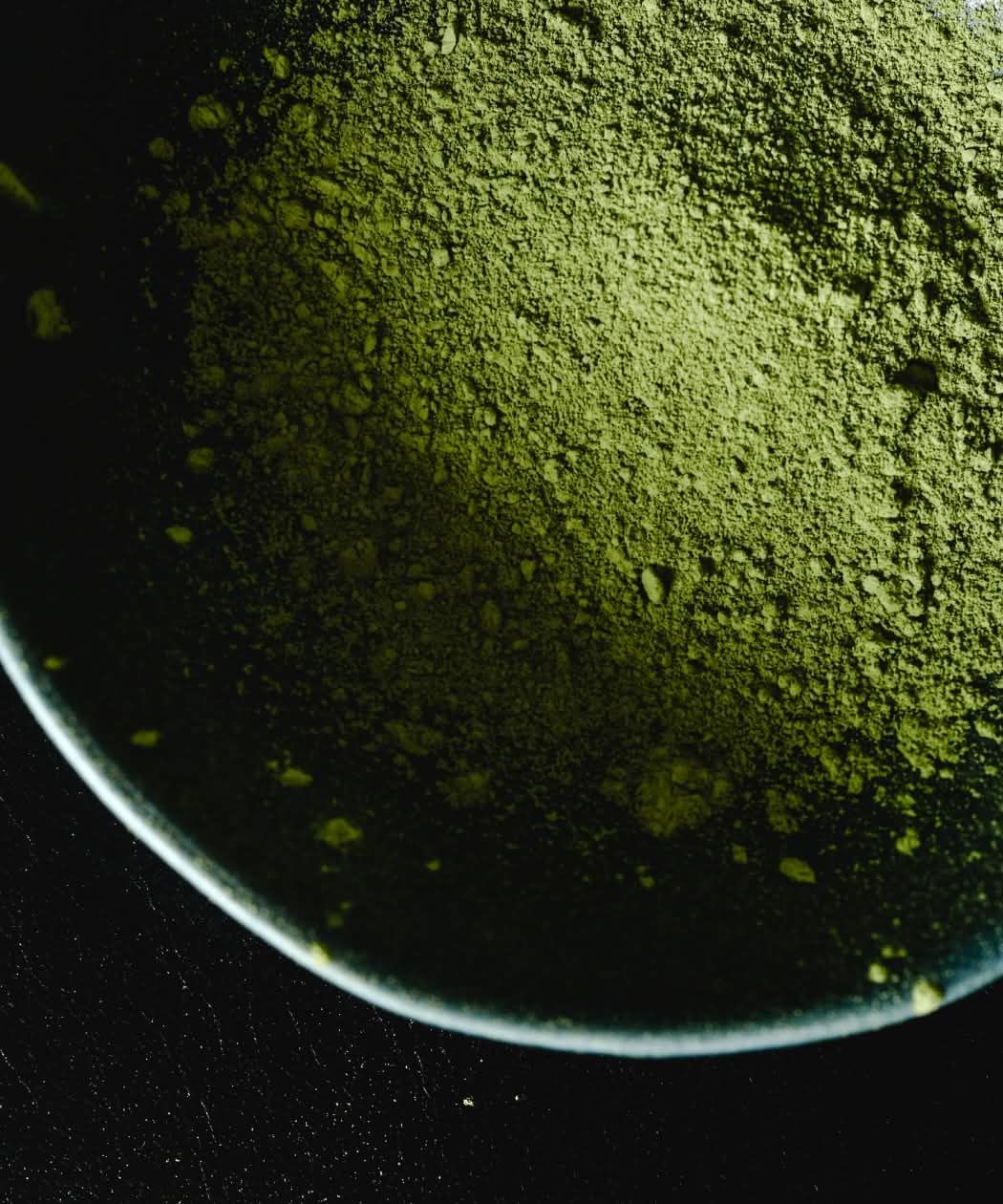 Green powder in a shallow dish on a dark background.
