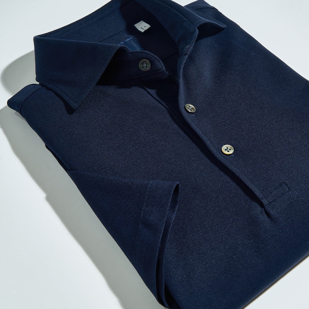 Folded navy blue shirt with buttons on a light background.
