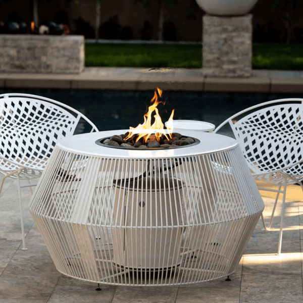 White round hidden propane tank fire pit with lava rocks on a poolside patio with white metal chairs