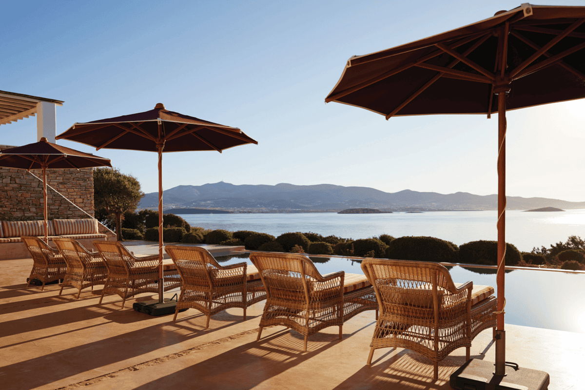 Outdoor wicker lounge chairs arranged beside an infinity pool with large patio umbrellas and mountain views.