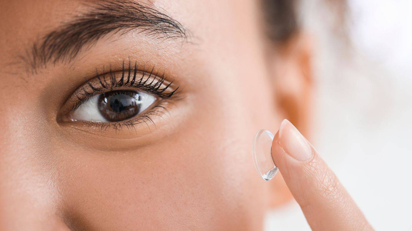A close up eye of a woman holding a contact lens on her finger