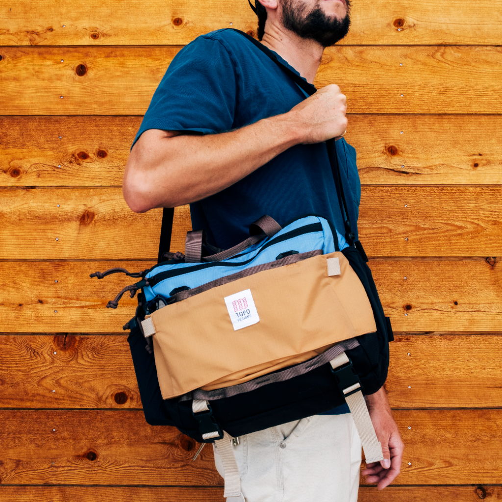 Man holding a messenger bag against a wooden wall background.