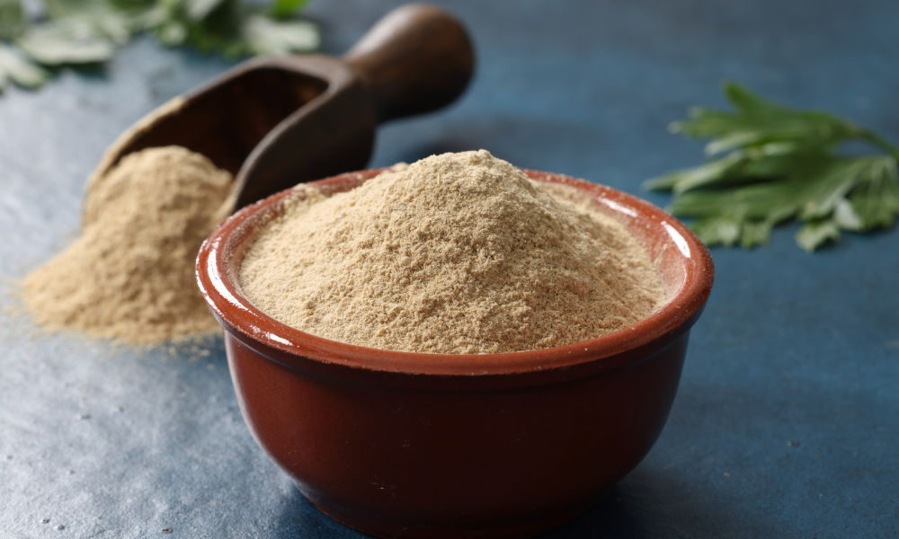 Bowl of ashwagandha with a wooden scoop and leaves.