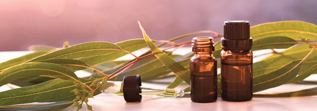 Amber bottles with essential oils beside green leaves on a surface.