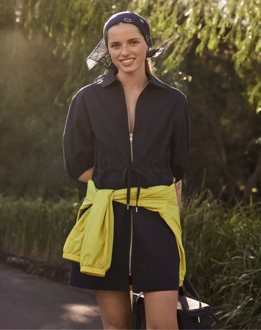 Smiling woman in a navy outfit with yellow accents and a headscarf.