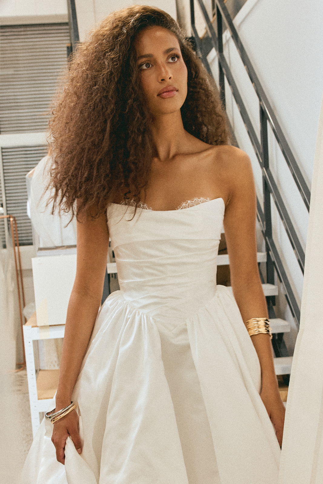 A woman in a white strapless dress stands indoors.