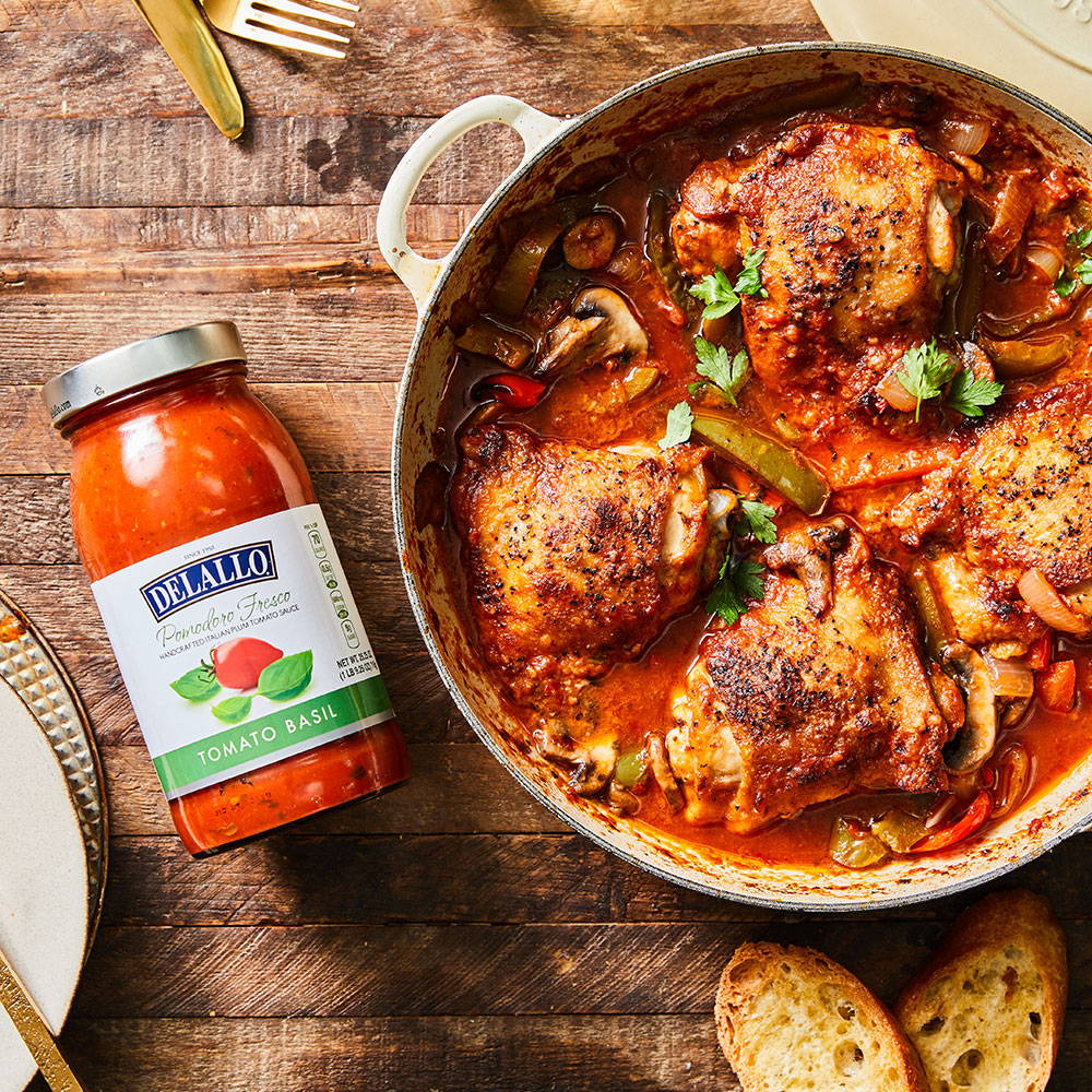Baked chicken in a pot of red sauce with peppers and mushrooms