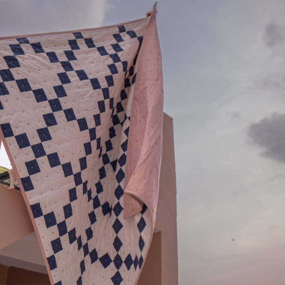 The Campbell Collection Rani Quilt in Indigo flapping in the wind with a stormy sky behind.