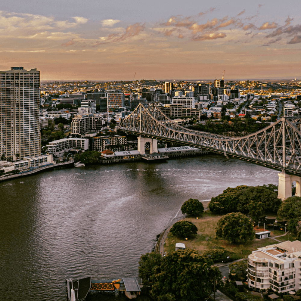 City skyline at sunset with a river and bridge.