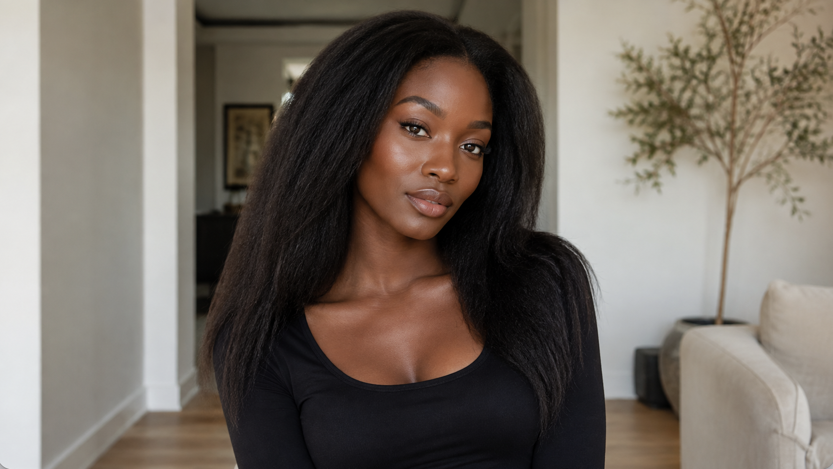 A woman with long hair poses indoors, wearing a black top.