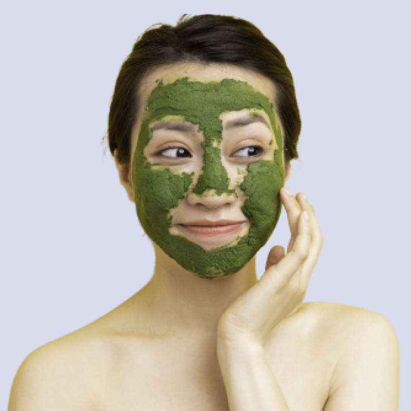 A woman applying a green facial mask , which covers most of her face