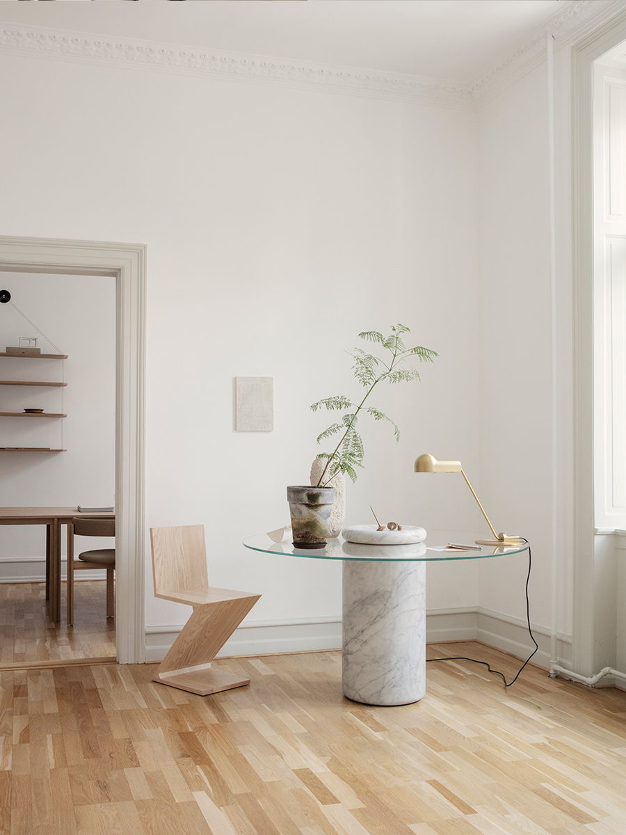 A minimalist interior with a glass table, plant, and wooden chair.