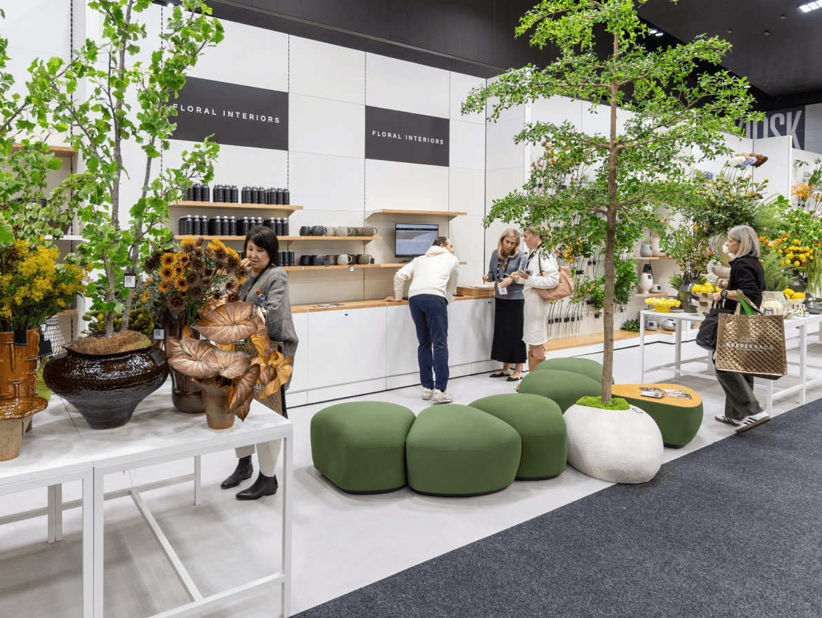 People interacting with greenery and furniture in a modern exhibition space.