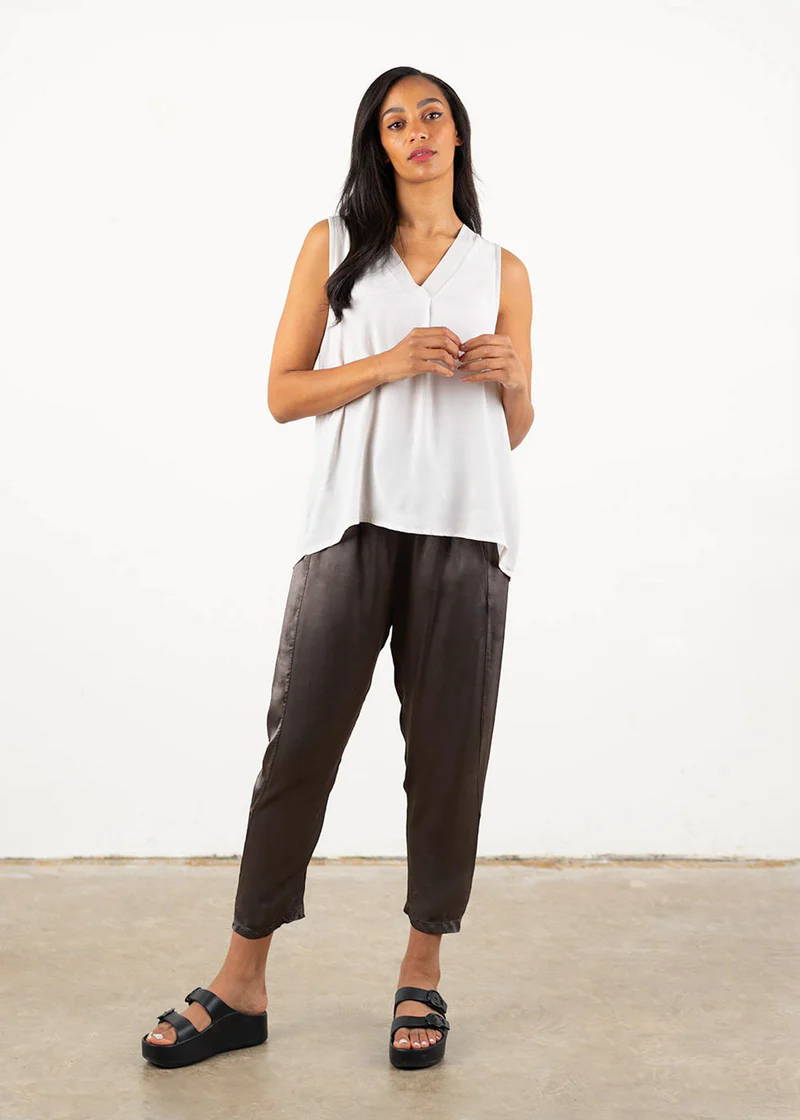 A model wearing a white sleeveless off white top with v neckline, dark grey satin trousers and black chunky slides