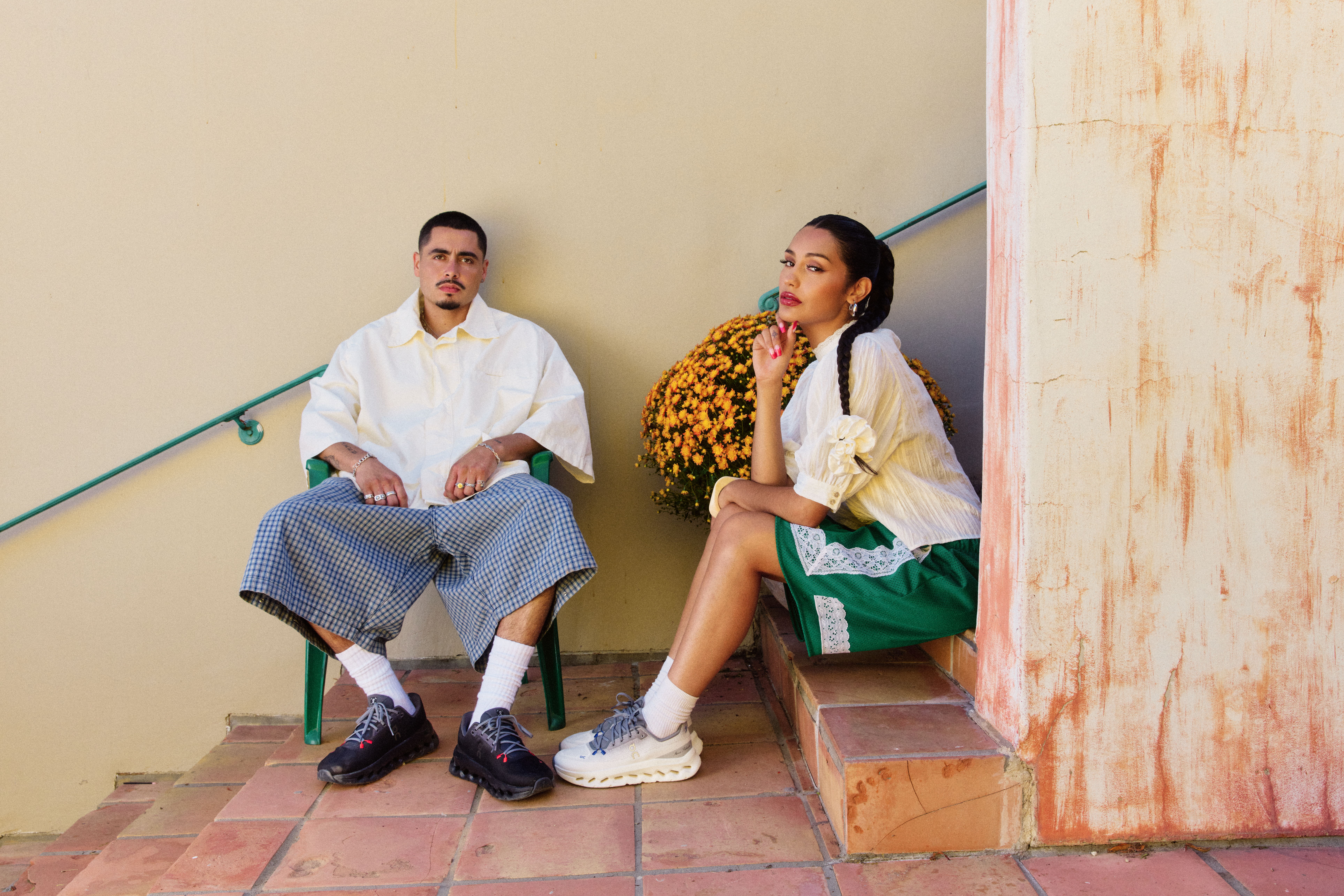 Two people sitting on steps, one wearing oversized shorts, the other in sportswear.
