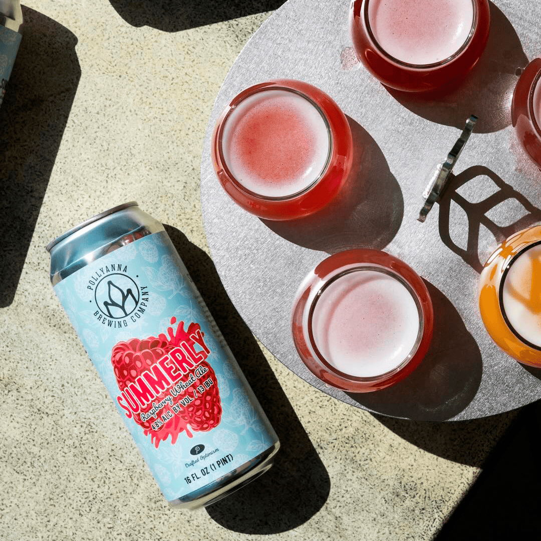 A can of summer beverage beside colorful glasses on a table.