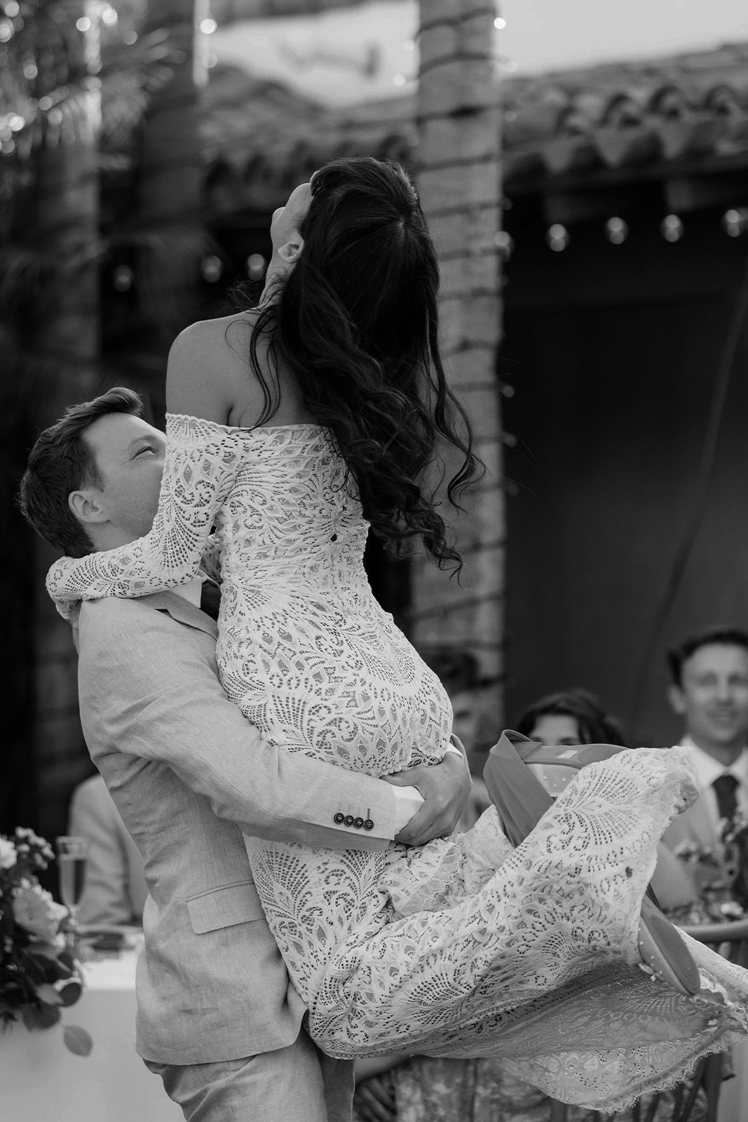 Couple celebrating at a wedding, man lifting woman in a white dress.