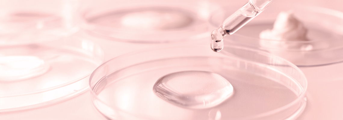 Pipette dropping liquid into petri dishes on a pink background.
