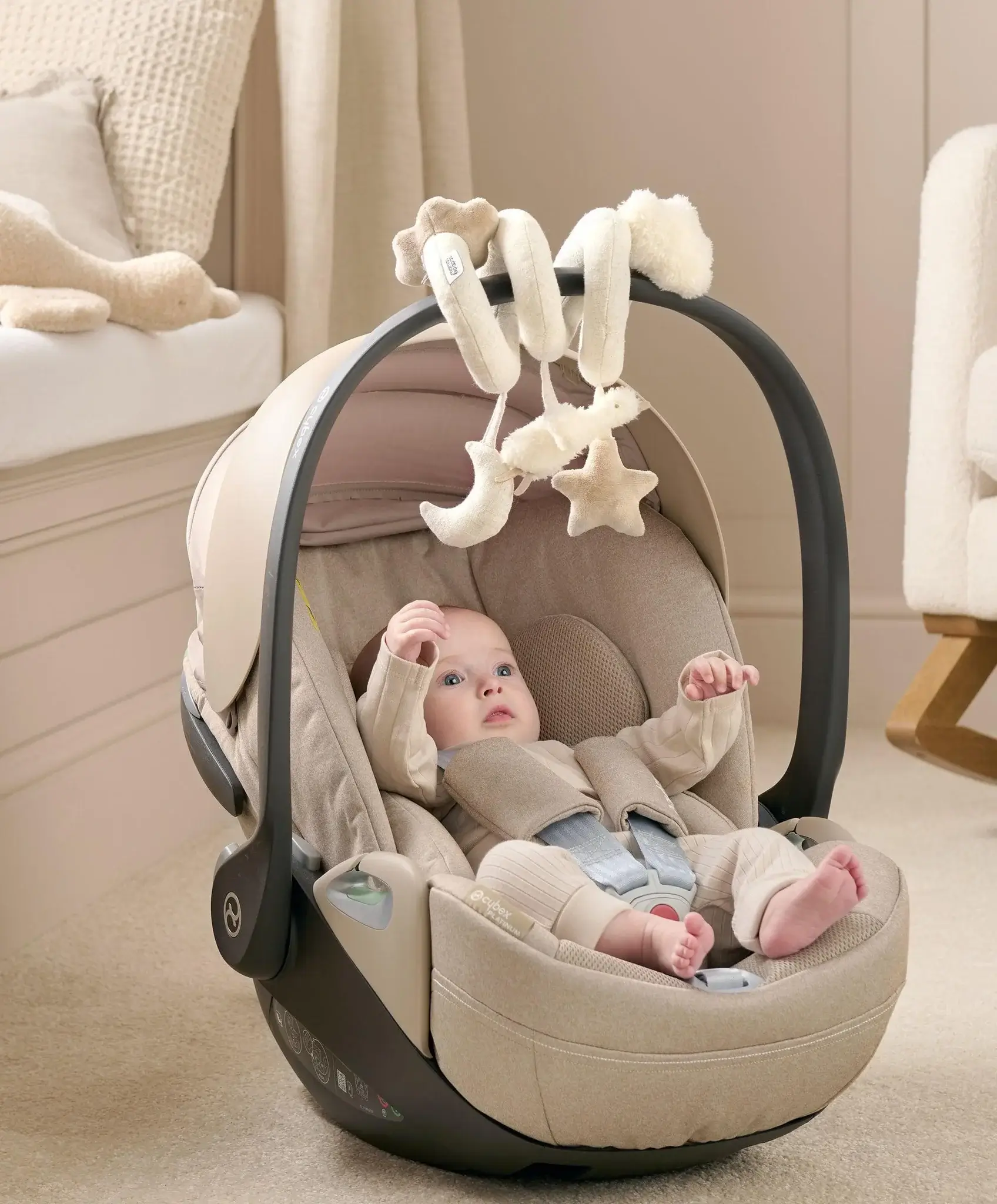 Baby in a car seat with hanging toys in a cozy room.