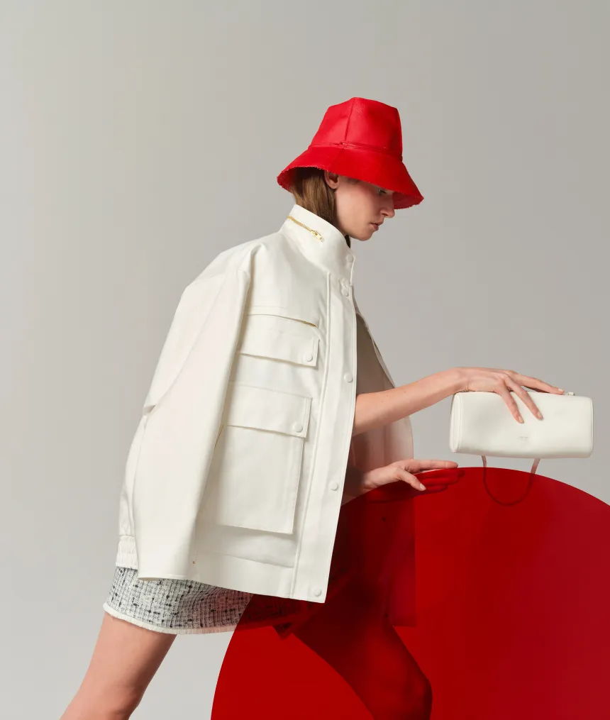 Model in white outfit and red bucket hat, leaning on red circle.