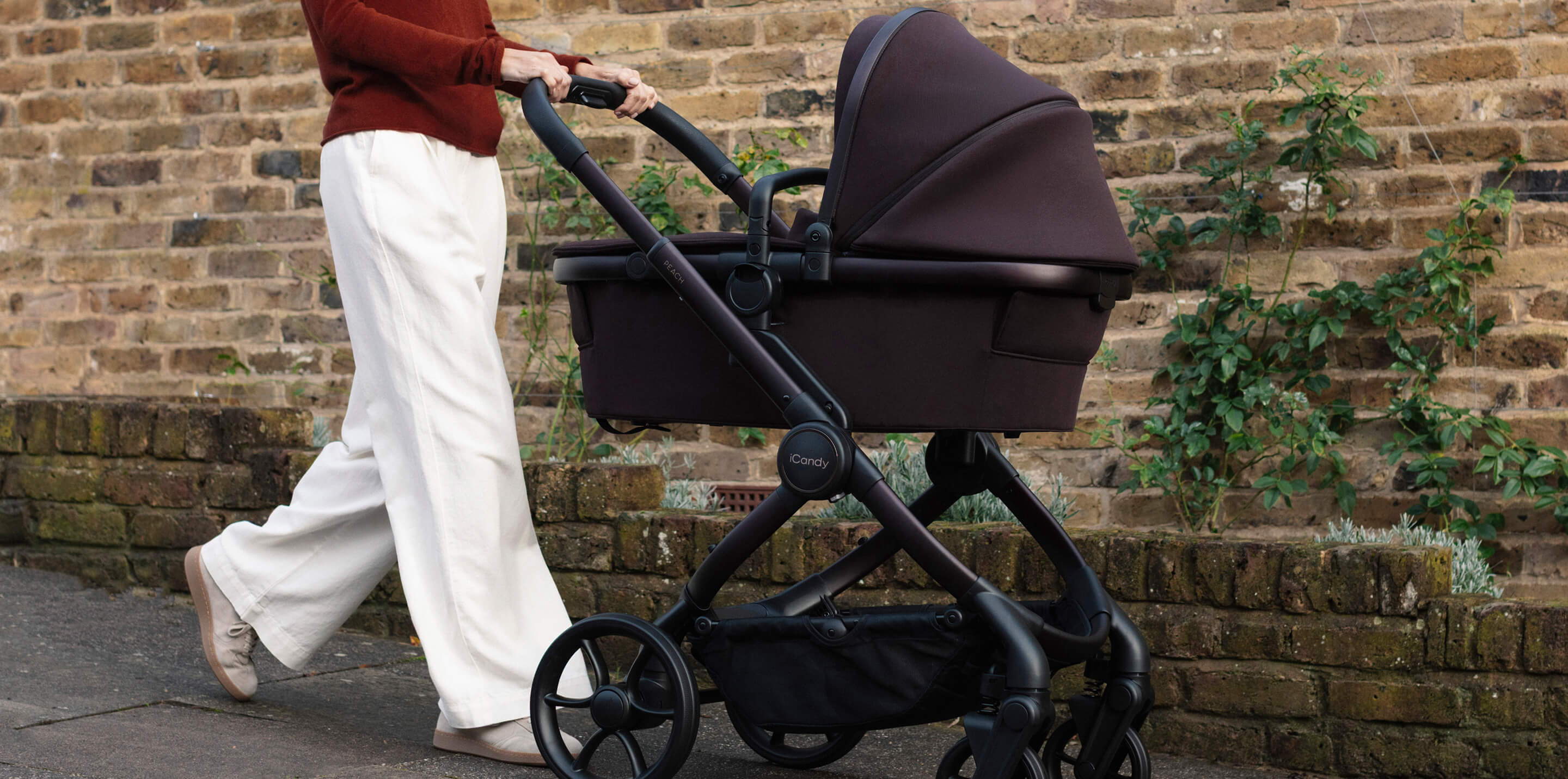 Person walking with a iCandy Peach 8 stroller on a sidewalk near a brick wall.