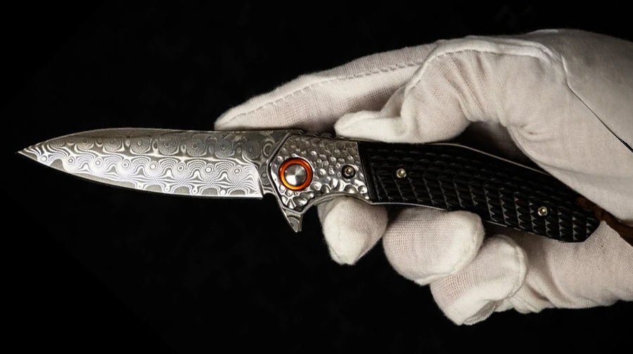 A hand in a glove holding an ornate knife with a patterned blade.