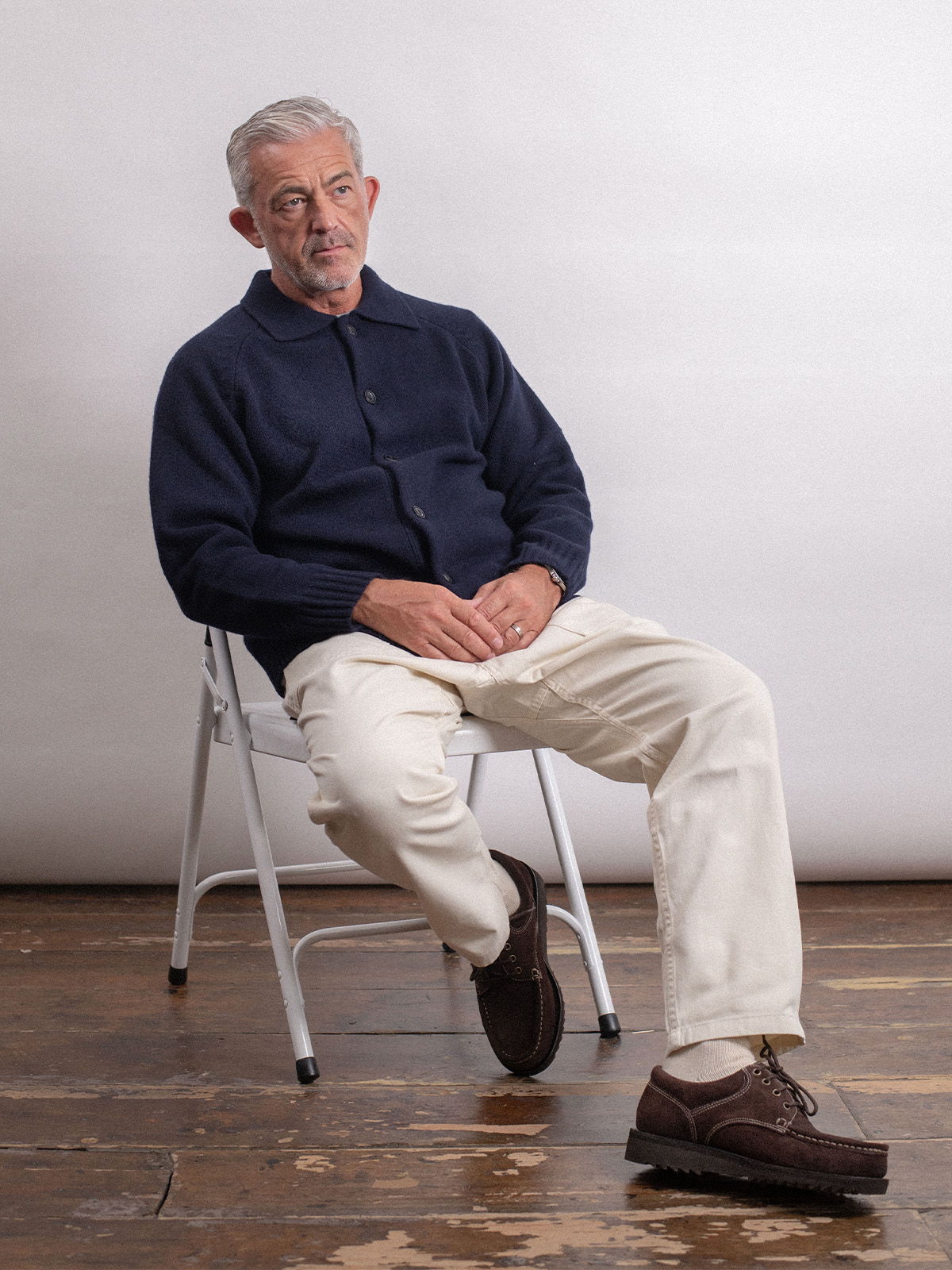 Rob sitting on a chair, wearing a navy sweater and beige pants.