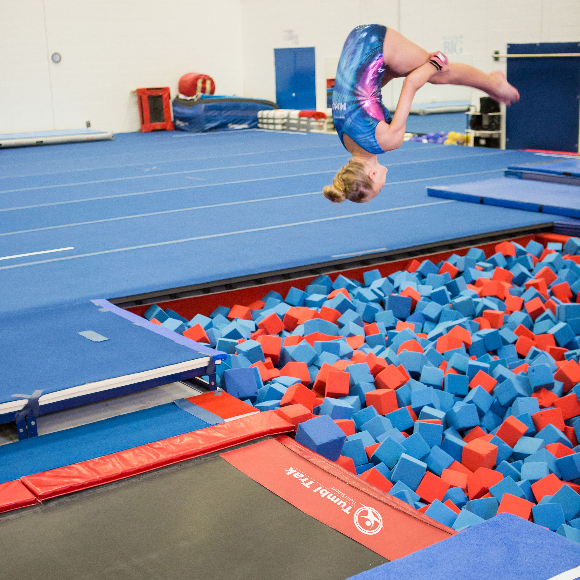 Gymnast performing a flip over a foam pit in a training facility.