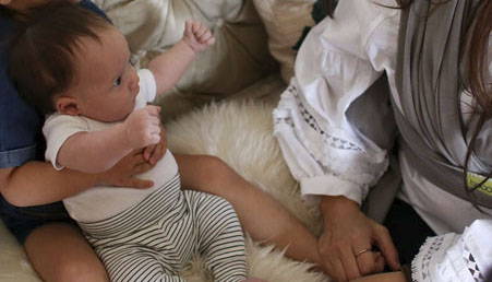 newborn-with-arms-up-held-by-brother-sitting-on-sheep-skin-rug