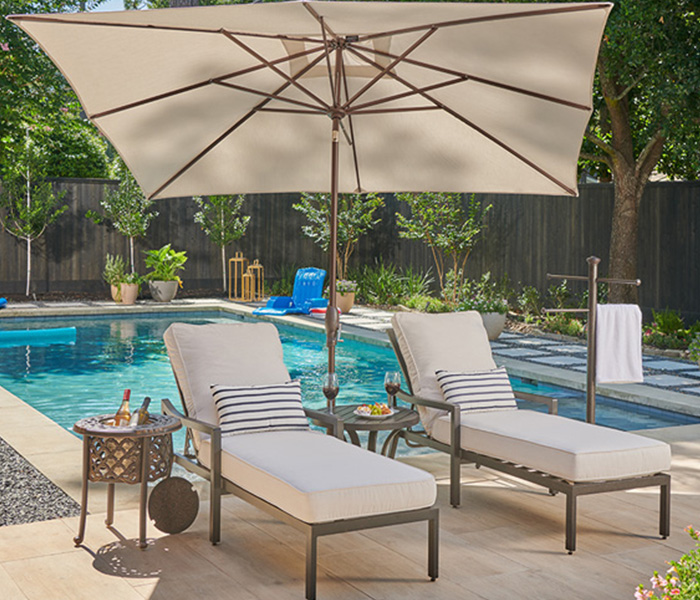 Lounge chairs by a pool with an umbrella and decorative plants.