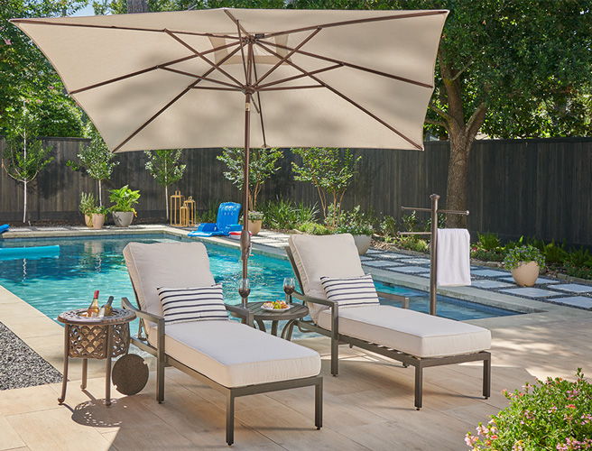 Two lounge chairs under an umbrella by a swimming pool.