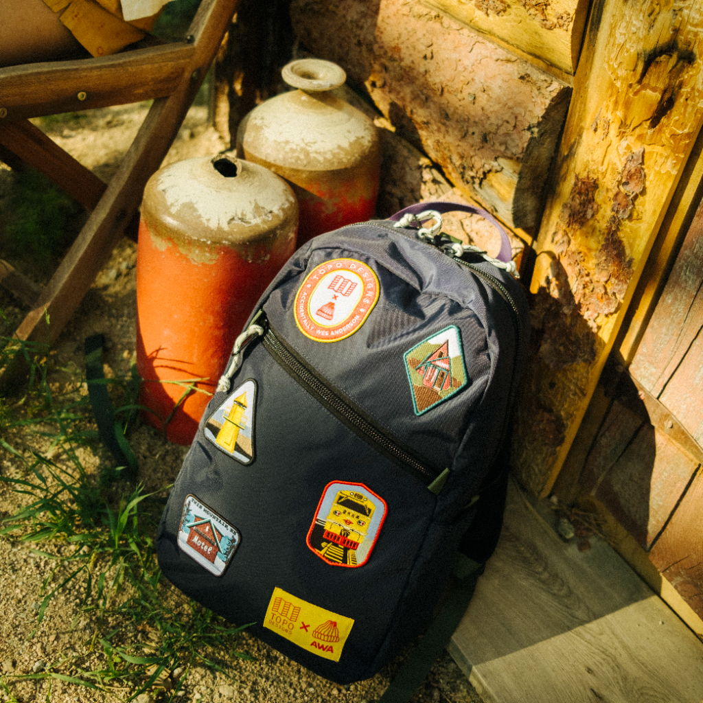 A black backpack with various colorful patches near two gas canisters.