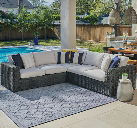 Outdoor sectional sofa with cushions near a swimming pool and dining area.
