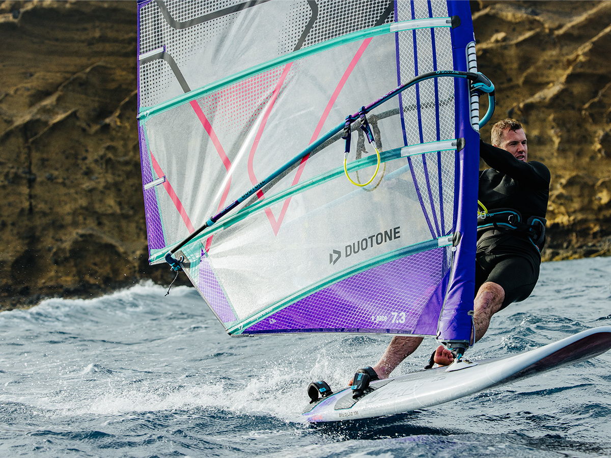 A person windsurfing on water near a rocky coastline.