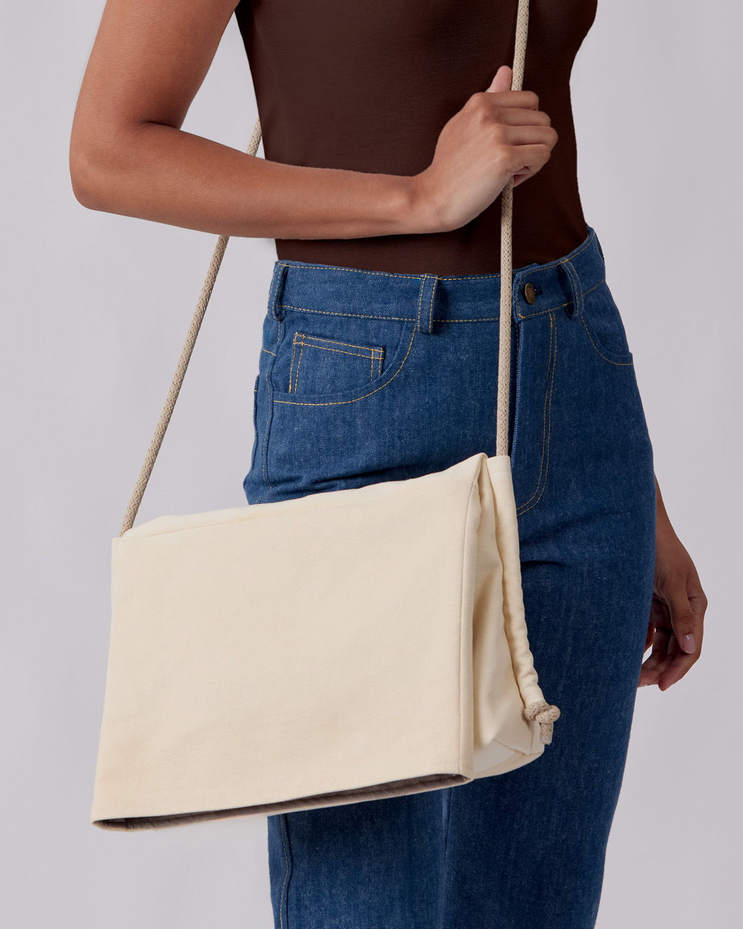 A person holding a cream-colored handbag against a neutral background.
