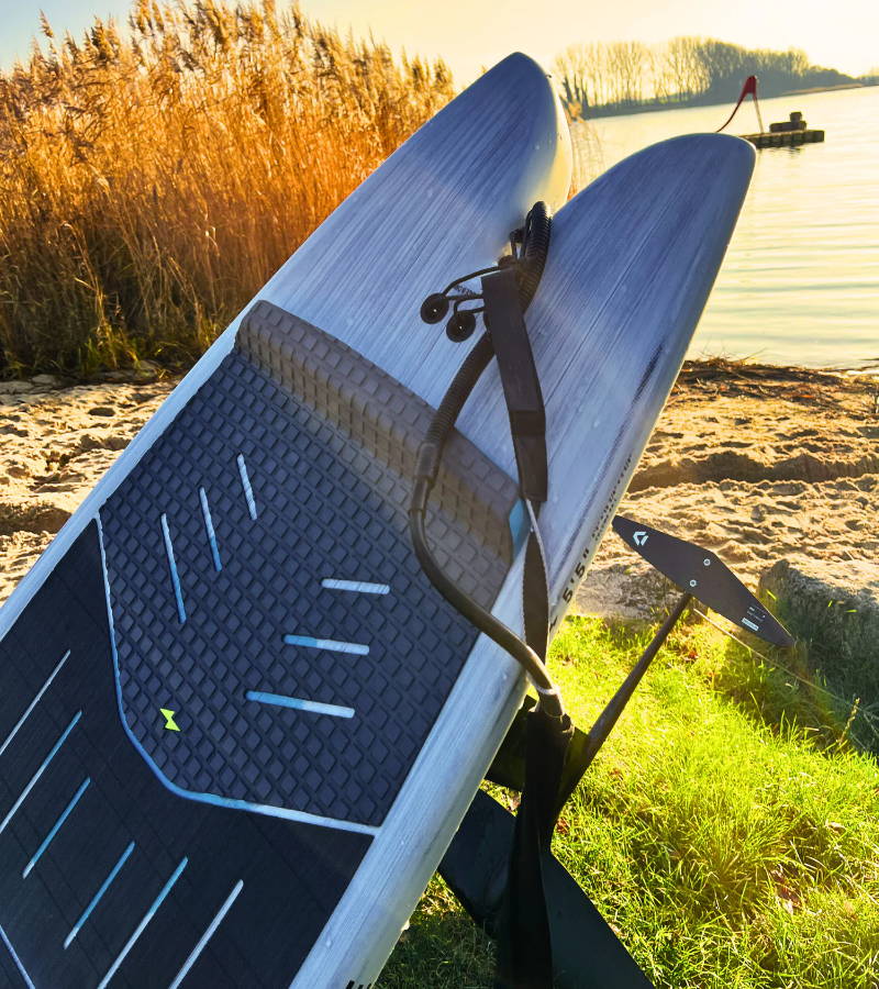 A surfboard with a foil on grass near the sea.