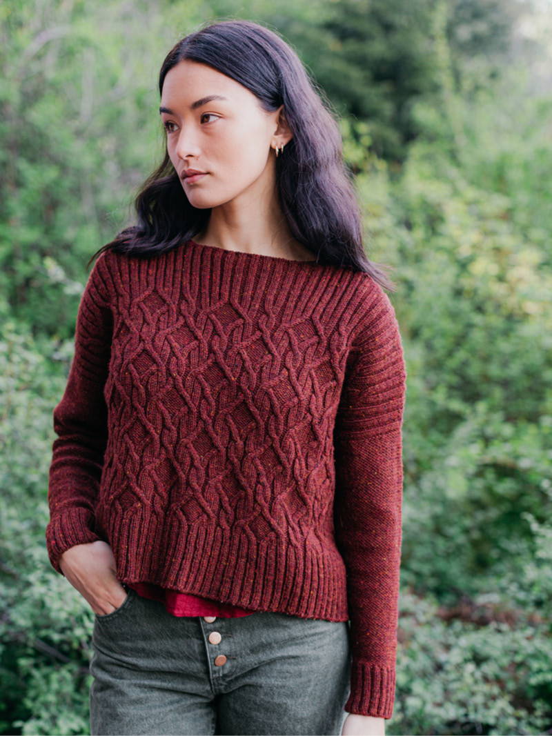 Candace, a woman, models a hand knit cabled pullover in Brooklyn Tweed Imbue Worsted yarn, color Cloak