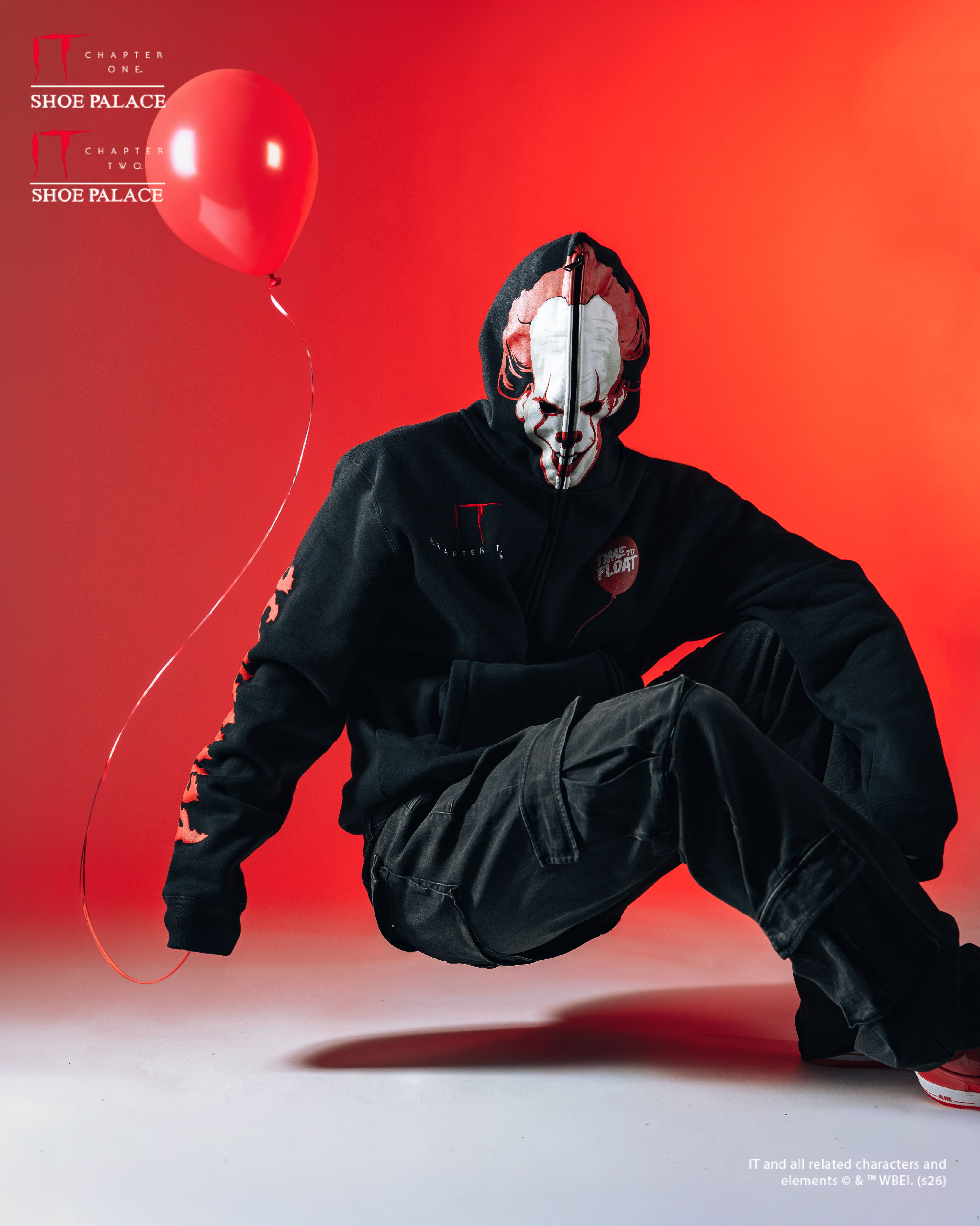 Person in a mask sitting with a red balloon against a red background.